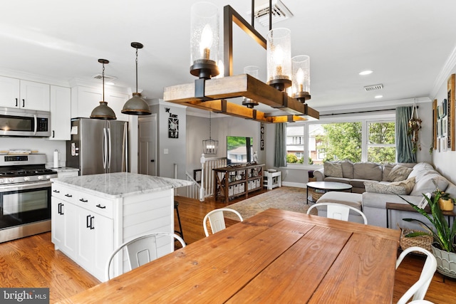 kitchen featuring appliances with stainless steel finishes, open floor plan, a chandelier, a center island, and ornamental molding