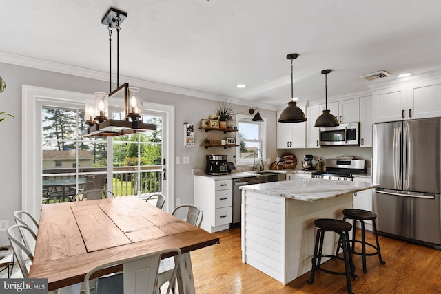 kitchen with stainless steel appliances, a sink, healthy amount of natural light, a center island, and crown molding