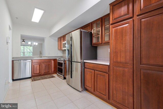 kitchen with appliances with stainless steel finishes, light countertops, a sink, glass insert cabinets, and brown cabinets