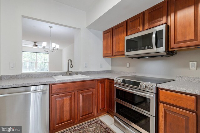kitchen featuring appliances with stainless steel finishes, a sink, a chandelier, and brown cabinetry