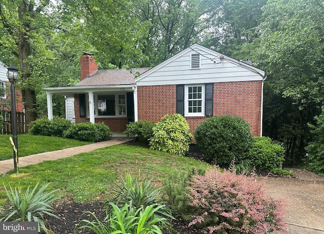 view of front of property featuring a chimney, brick siding, covered porch, and a front lawn
