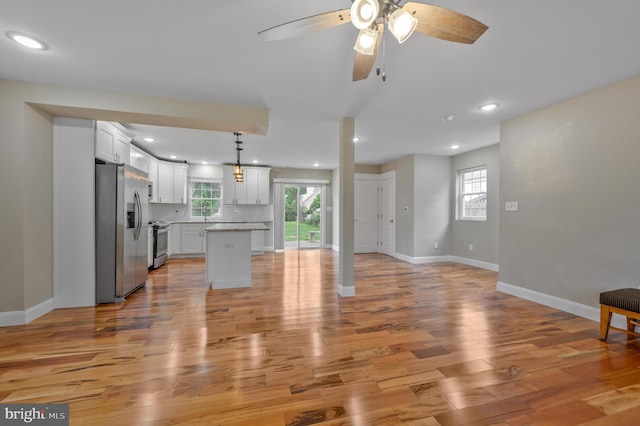 unfurnished living room with plenty of natural light, light wood-style floors, a ceiling fan, baseboards, and recessed lighting