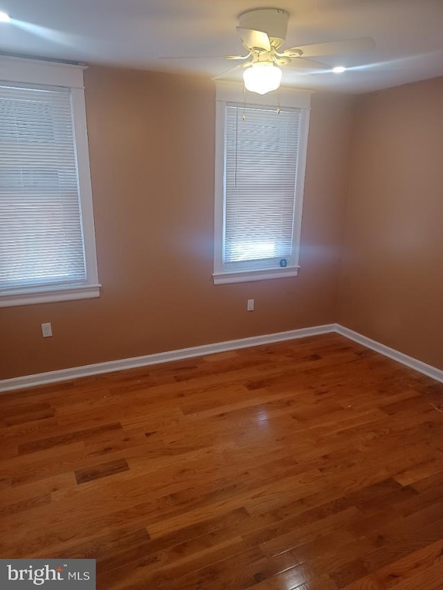 empty room with wood finished floors, a ceiling fan, baseboards, and plenty of natural light
