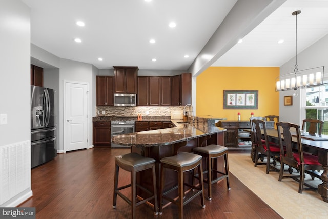 kitchen featuring stainless steel appliances, a sink, a peninsula, a breakfast bar, and tasteful backsplash