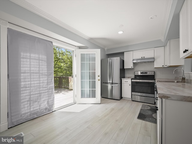 kitchen with appliances with stainless steel finishes, under cabinet range hood, a sink, ornamental molding, and white cabinets