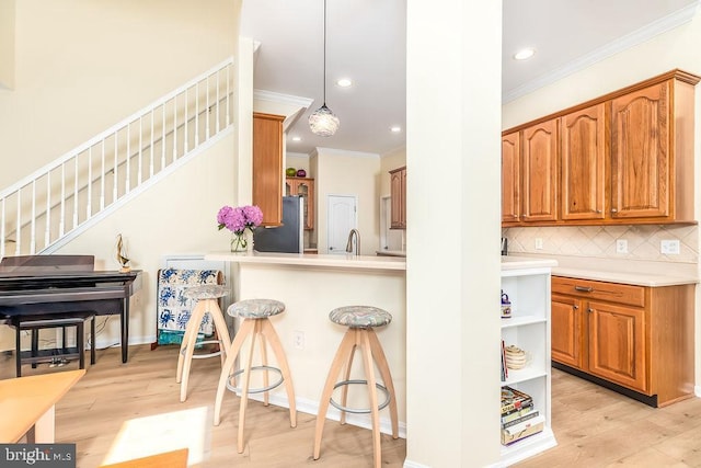 111 Central Parke E, Ocean Pines, MD 21811 - kitchen with ornamental molding, freestanding refrigerator, a breakfast bar area, decorative backsplash, and light wood-style flooring