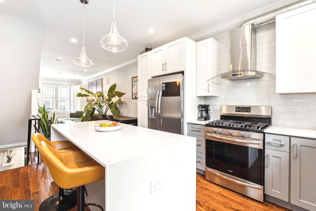 kitchen with appliances with stainless steel finishes, wall chimney exhaust hood, crown molding, a kitchen island, and light countertops