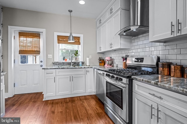 kitchen featuring appliances with stainless steel finishes, wall chimney range hood, a sink, dark stone counters, and recessed lighting