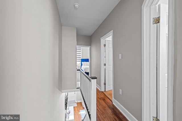 hallway with an upstairs landing, wood finished floors, and baseboards