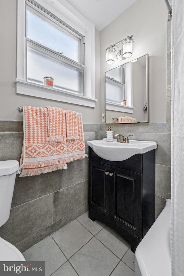 full bathroom with tile walls, tile patterned floors, toilet, a wainscoted wall, and vanity
