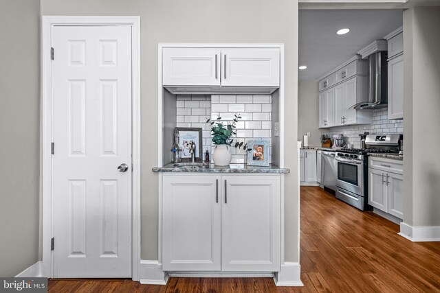 kitchen featuring appliances with stainless steel finishes, wall chimney exhaust hood, decorative backsplash, dark wood-type flooring, and recessed lighting