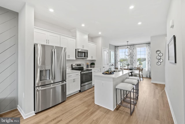 kitchen with stainless steel appliances, white cabinets, a center island with sink, baseboards, and light countertops