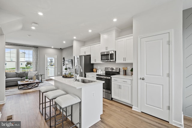 kitchen featuring appliances with stainless steel finishes, a sink, a kitchen breakfast bar, a center island with sink, and white cabinetry