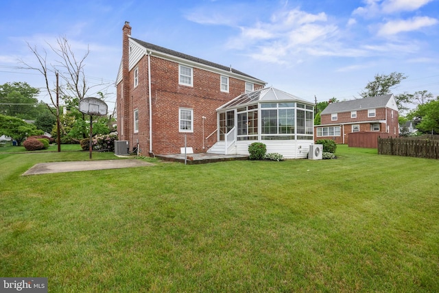 rear view of property featuring a chimney, brick siding, a patio area, a sunroom, and a cooling unit