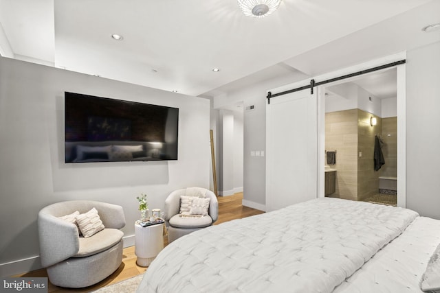bedroom featuring a barn door, baseboards, recessed lighting, ensuite bathroom, and wood finished floors