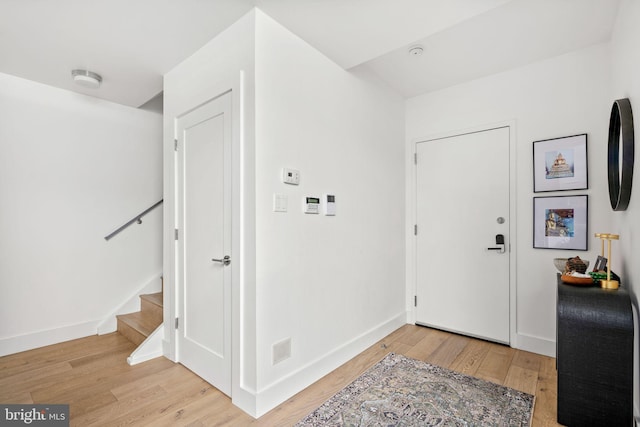 foyer entrance featuring light wood-type flooring, baseboards, and stairs