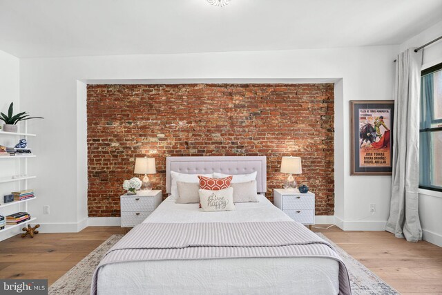 bedroom with baseboards, light wood-style flooring, and brick wall