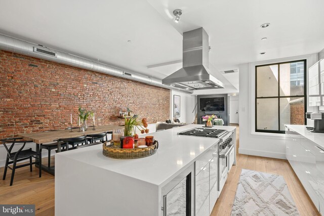 kitchen with extractor fan, brick wall, stainless steel stove, light wood-style floors, and beverage cooler