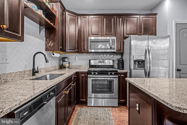 kitchen featuring stainless steel appliances, a sink, dark brown cabinetry, and light stone countertops