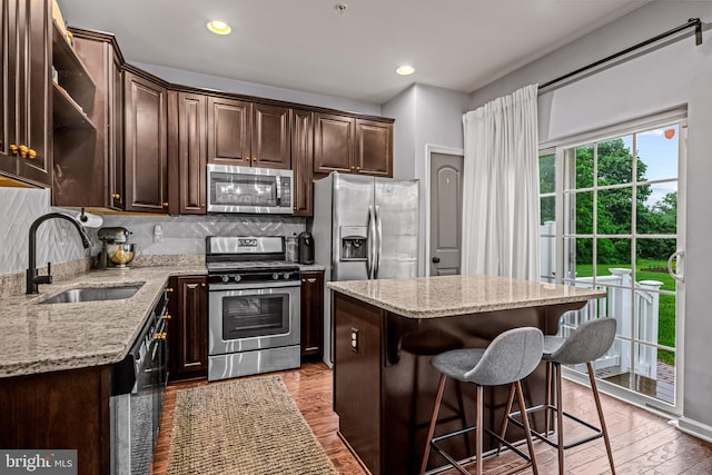 kitchen with appliances with stainless steel finishes, a sink, dark brown cabinetry, light stone countertops, and a kitchen island