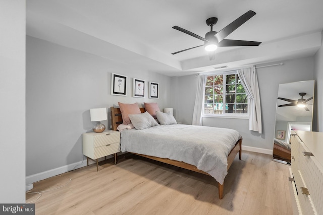 bedroom with light wood finished floors, baseboards, ceiling fan, and a tray ceiling