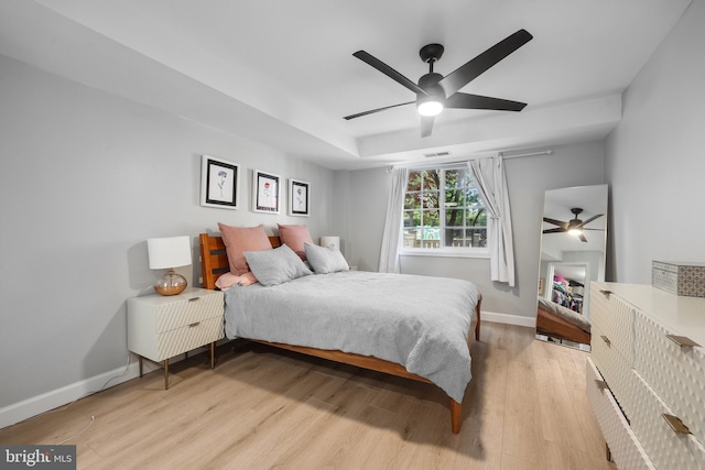 bedroom featuring light wood-type flooring, baseboards, ceiling fan, and a tray ceiling