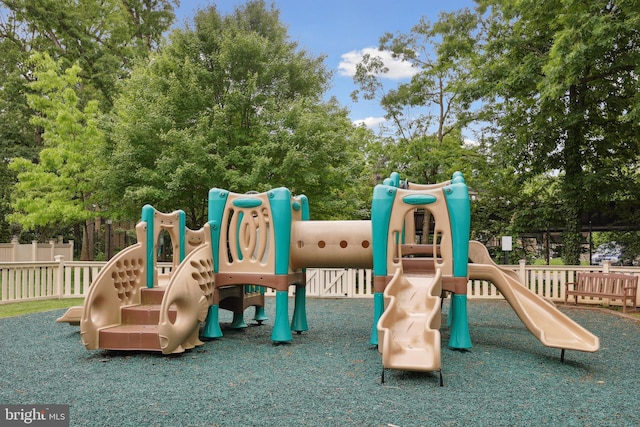 community play area featuring fence and view of wooded area