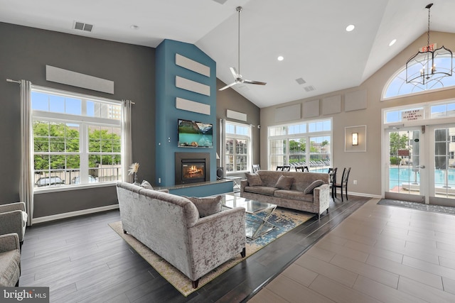 living area featuring plenty of natural light, high vaulted ceiling, ceiling fan, a glass covered fireplace, and baseboards