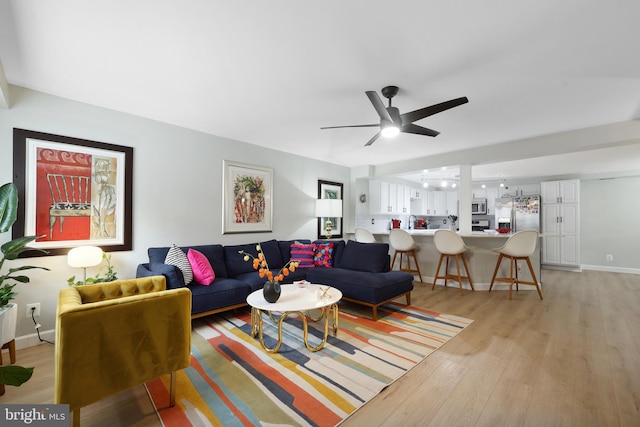 living area featuring light wood finished floors, ceiling fan, and baseboards