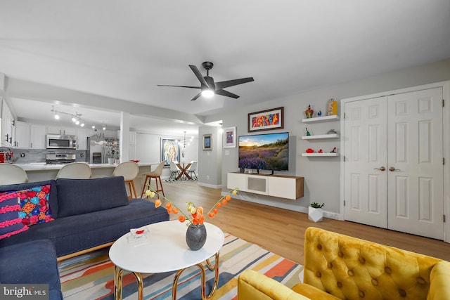 living room with a ceiling fan, light wood-type flooring, baseboards, and a chandelier