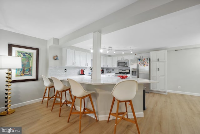 kitchen with appliances with stainless steel finishes, a peninsula, light wood-style flooring, and white cabinetry