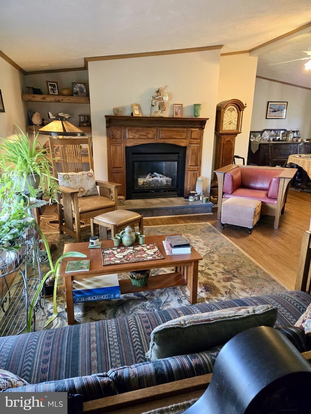 living area with ornamental molding, wood finished floors, a glass covered fireplace, and lofted ceiling