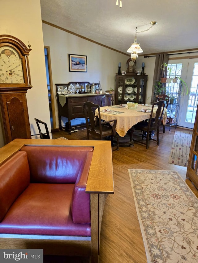 dining area with lofted ceiling, crown molding, wood finished floors, and a textured ceiling