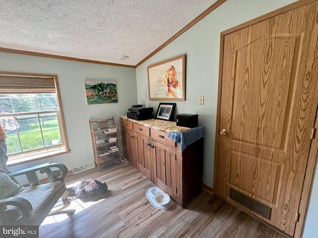 office area featuring a textured ceiling, light wood-type flooring, ornamental molding, and vaulted ceiling