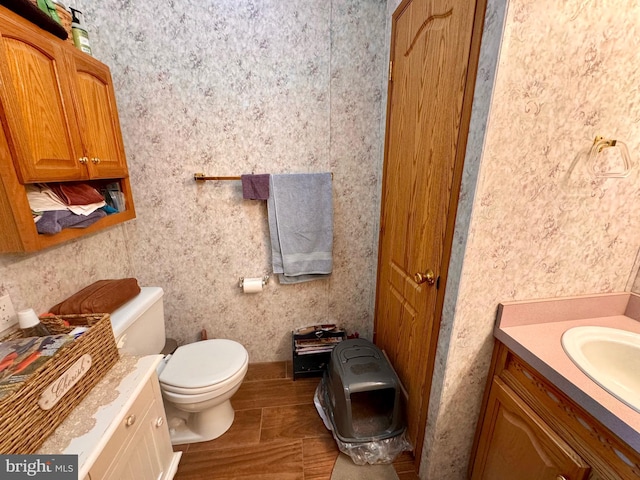 bathroom with vanity, toilet, and wallpapered walls