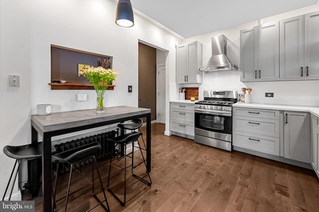 kitchen featuring stainless steel range with gas cooktop, wall chimney range hood, dark wood-style flooring, and light countertops