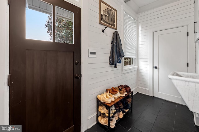 mudroom with wood walls, healthy amount of natural light, and dark tile patterned floors