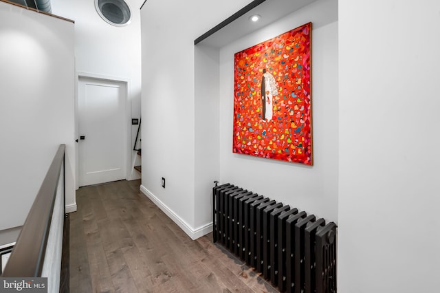 hall with radiator, wood finished floors, baseboards, recessed lighting, and an upstairs landing