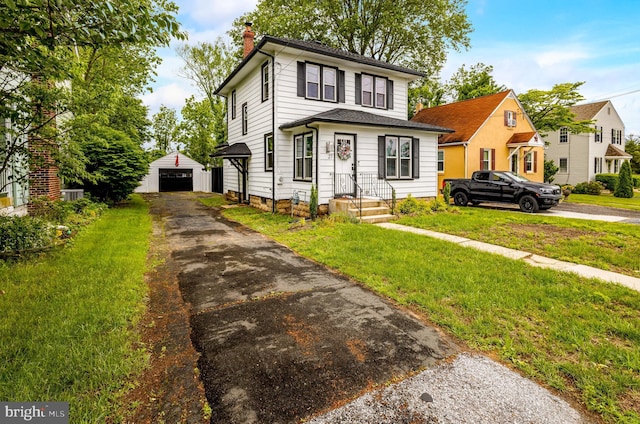 american foursquare style home with a chimney, a detached garage, an outbuilding, driveway, and a front yard
