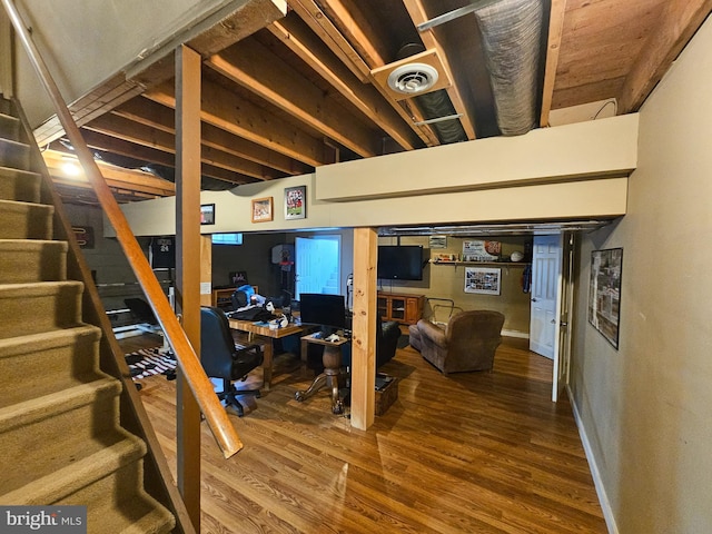 finished basement with wood finished floors, a desk, stairway, and baseboards