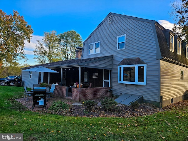 rear view of house with a sunroom, a yard, a chimney, a gambrel roof, and a shingled roof