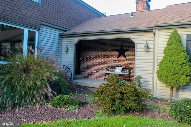 entrance to property featuring a shingled roof and a chimney