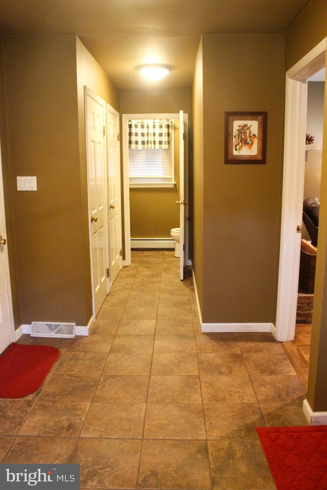 hallway featuring baseboard heating, baseboards, and tile patterned floors