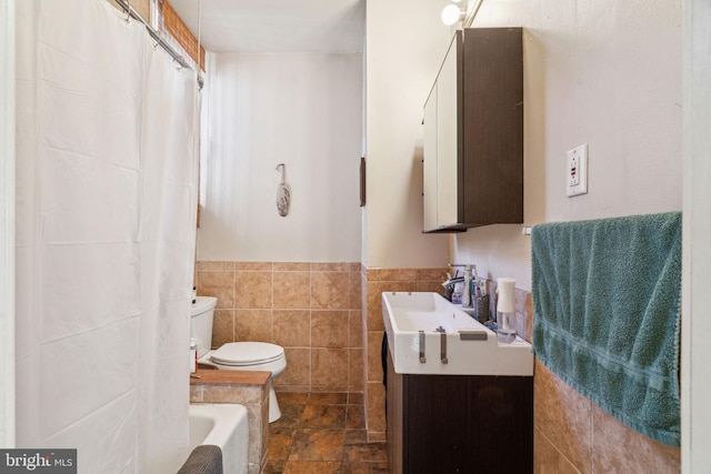 bathroom with toilet, tile walls, wainscoting, vanity, and stone finish flooring