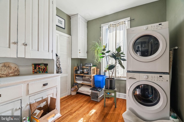 laundry room with stacked washer / dryer, light wood-type flooring, cabinet space, and baseboards