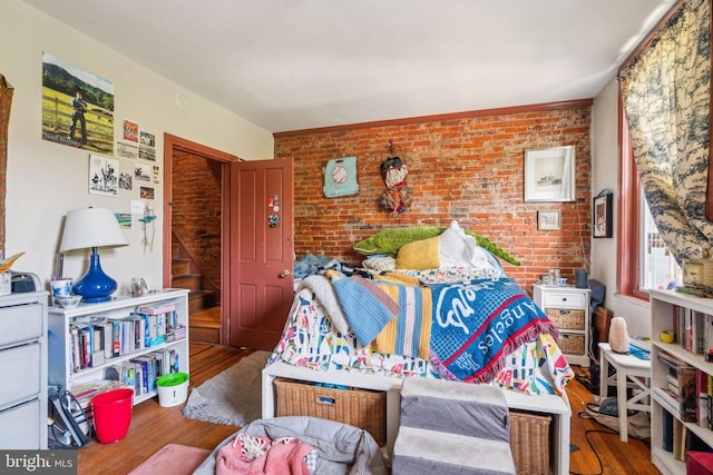 bedroom with wood finished floors and brick wall