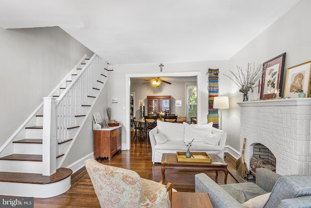 living area featuring stairway, dark wood-style flooring, baseboards, a fireplace, and a ceiling fan