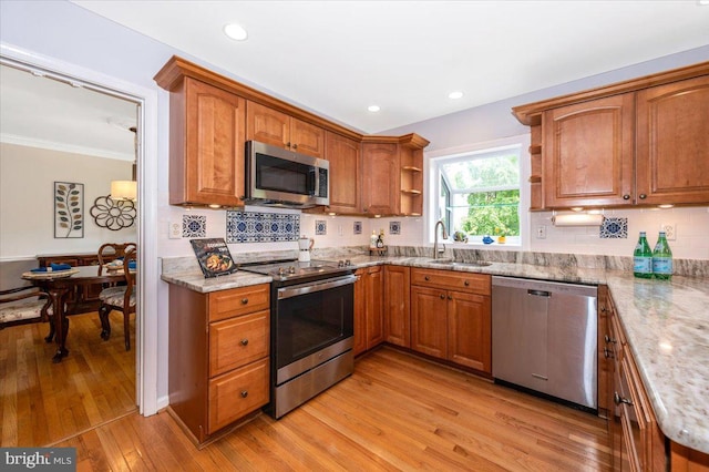 kitchen with appliances with stainless steel finishes, open shelves, a sink, light wood finished floors, and light stone countertops