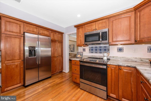 kitchen with appliances with stainless steel finishes, light wood finished floors, tasteful backsplash, light stone countertops, and brown cabinets