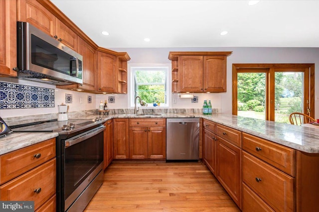kitchen with stainless steel appliances, a sink, open shelves, light stone countertops, and a peninsula